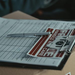 A clipboard with delivery papers and a 'Handle with Care' sticker on a cardboard box.